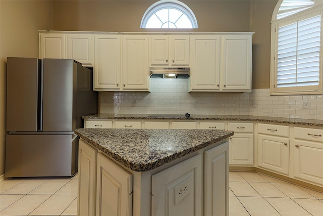 kitchen with light tile patterned floors, a kitchen island, freestanding refrigerator, decorative backsplash, and under cabinet range hood