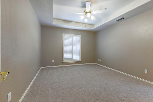 spare room with visible vents, a ceiling fan, a tray ceiling, carpet, and baseboards