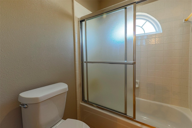 full bathroom with toilet, a textured wall, and shower / bath combination with glass door