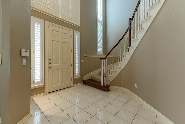 foyer entrance featuring stairway, light tile patterned floors, baseboards, and a towering ceiling