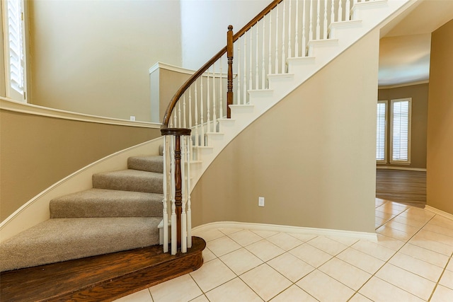 staircase featuring tile patterned flooring, a high ceiling, and baseboards