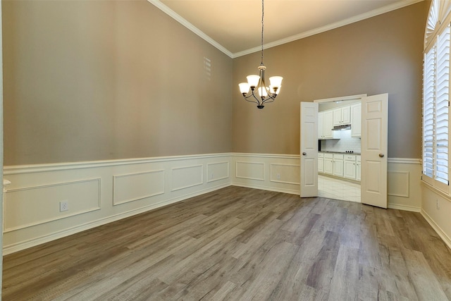 unfurnished dining area with a notable chandelier, wood finished floors, wainscoting, and ornamental molding