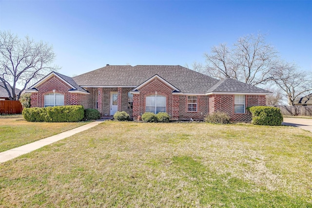 ranch-style home with brick siding, a shingled roof, a front yard, and fence