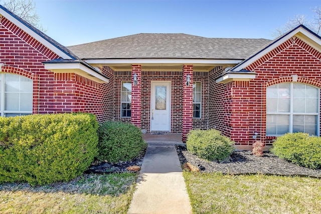 view of exterior entry with brick siding, an attached garage, and a shingled roof