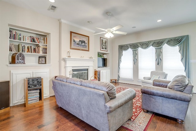 living room with visible vents, built in shelves, a glass covered fireplace, and wood finished floors