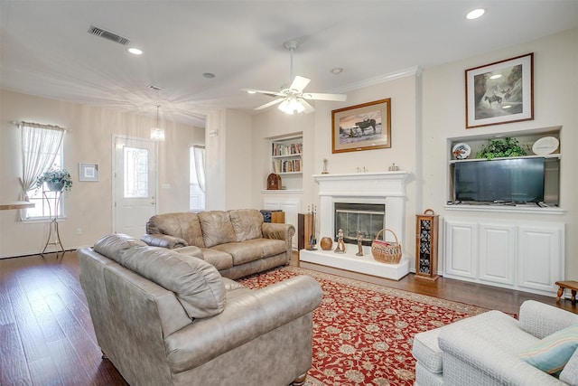 living room with visible vents, built in features, a glass covered fireplace, wood finished floors, and recessed lighting