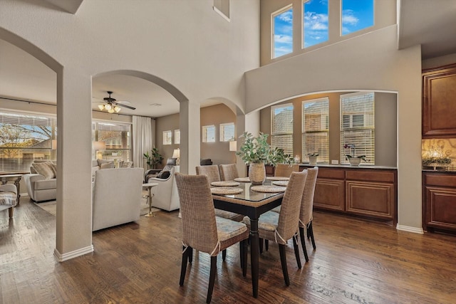 dining space featuring arched walkways, a ceiling fan, and dark wood-style flooring