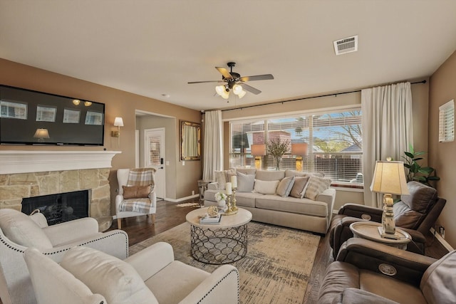 living area with wood finished floors, a ceiling fan, visible vents, baseboards, and a stone fireplace