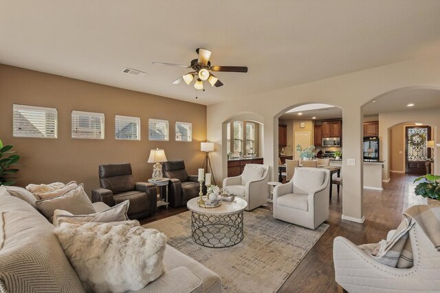 living room featuring a ceiling fan, wood finished floors, visible vents, baseboards, and arched walkways