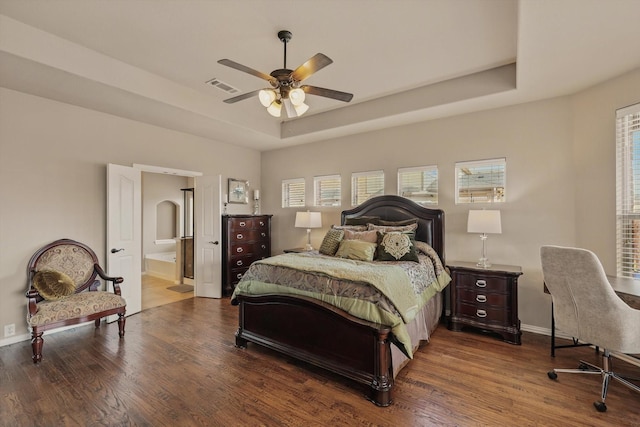 bedroom with visible vents, a tray ceiling, wood finished floors, connected bathroom, and baseboards