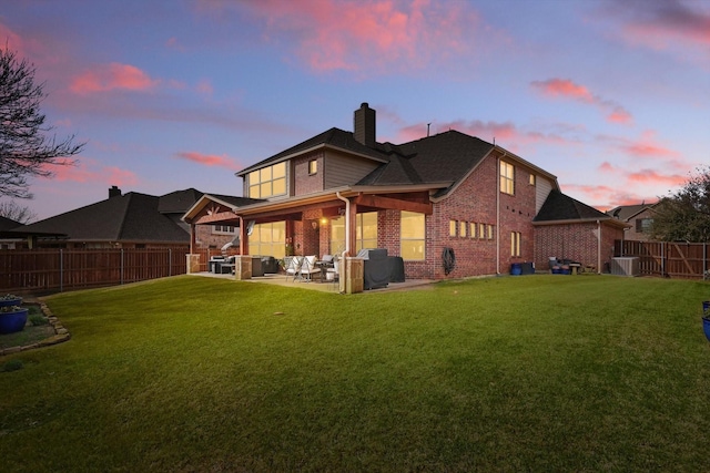 back of house at dusk with brick siding, a patio area, and a yard