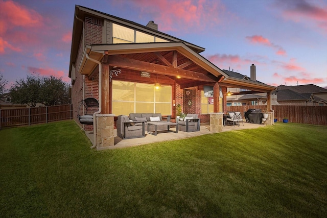 back of house at dusk featuring brick siding, an outdoor living space, a lawn, a chimney, and a patio