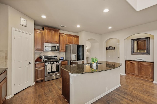 kitchen featuring visible vents, an island with sink, dark stone countertops, stainless steel appliances, and dark wood-style flooring