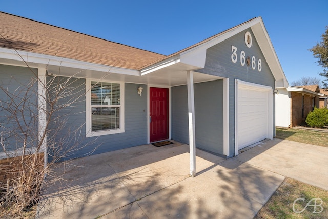 doorway to property with an attached garage, driveway, and roof with shingles