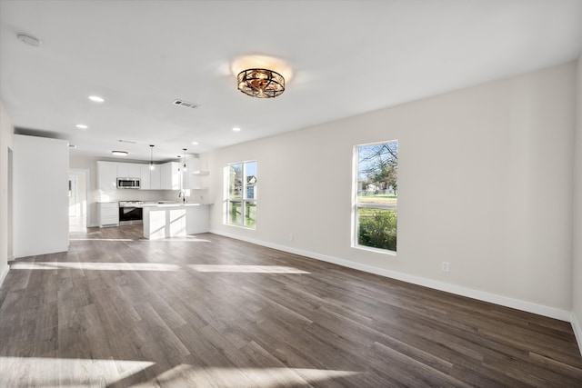 unfurnished living room featuring visible vents, baseboards, a healthy amount of sunlight, and dark wood-style flooring