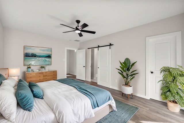 bedroom featuring ceiling fan, a barn door, baseboards, and wood finished floors