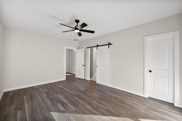 unfurnished bedroom with a barn door, wood finished floors, and baseboards