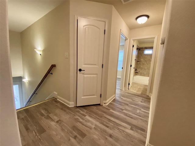 hallway featuring baseboards, an upstairs landing, and wood finished floors