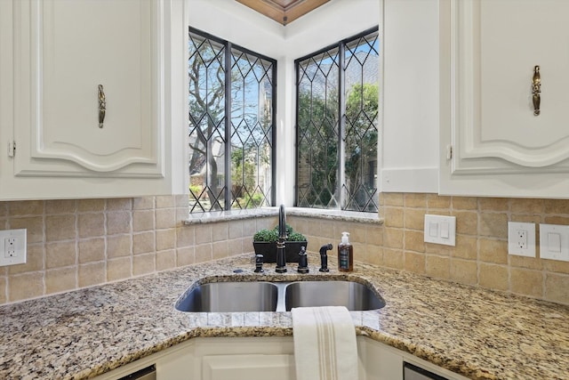 kitchen featuring light stone counters, decorative backsplash, white cabinetry, and a sink