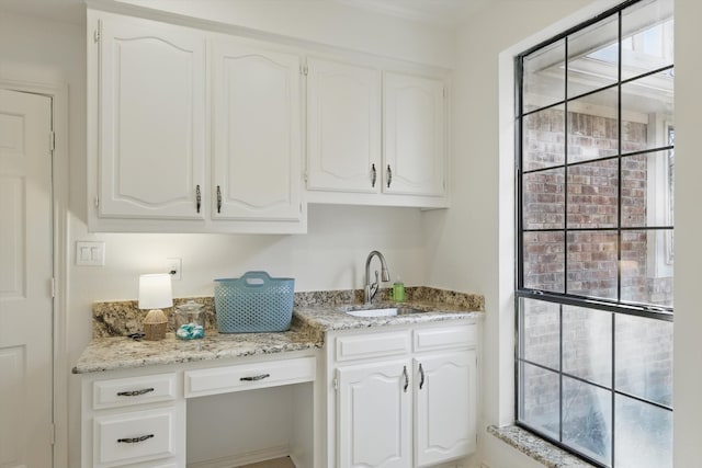 kitchen with light stone counters, white cabinetry, and a sink