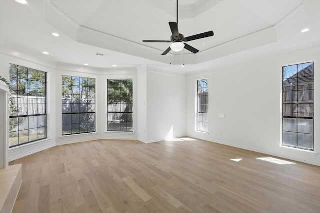 empty room with a raised ceiling, light wood-style flooring, a ceiling fan, recessed lighting, and baseboards