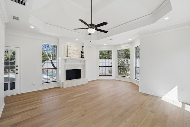 unfurnished living room with visible vents, a fireplace with raised hearth, light wood-style flooring, and a tray ceiling