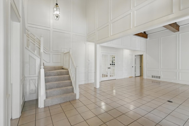 interior space with light tile patterned floors, visible vents, beam ceiling, stairs, and a decorative wall