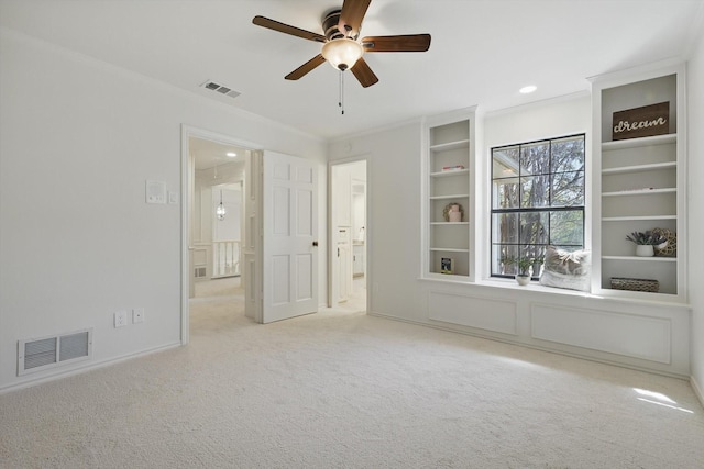 carpeted empty room featuring built in features, visible vents, and crown molding