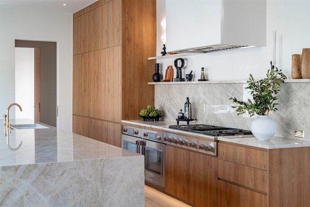 kitchen featuring modern cabinets, a sink, range hood, appliances with stainless steel finishes, and decorative backsplash