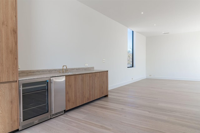 bar with beverage cooler, baseboards, light wood-style flooring, refrigerator, and a sink