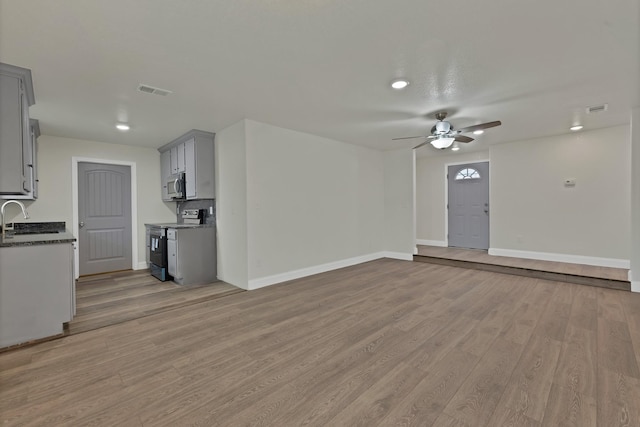 unfurnished living room with a ceiling fan, light wood-style floors, visible vents, and baseboards