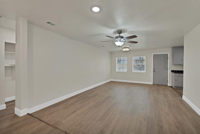 unfurnished living room featuring ceiling fan, visible vents, baseboards, and wood finished floors