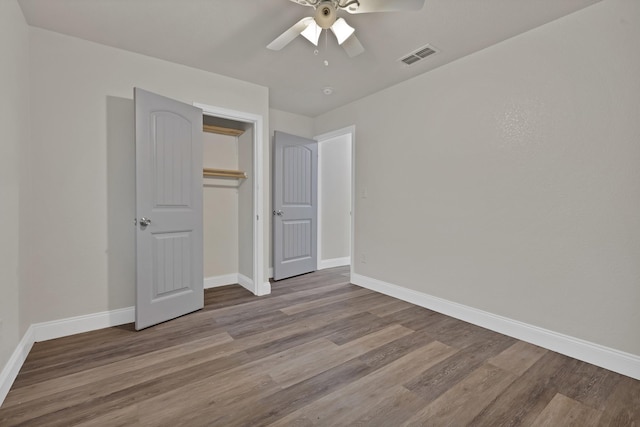 unfurnished bedroom with a ceiling fan, visible vents, wood finished floors, baseboards, and a closet