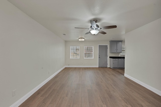 unfurnished living room with a ceiling fan, visible vents, wood finished floors, and baseboards