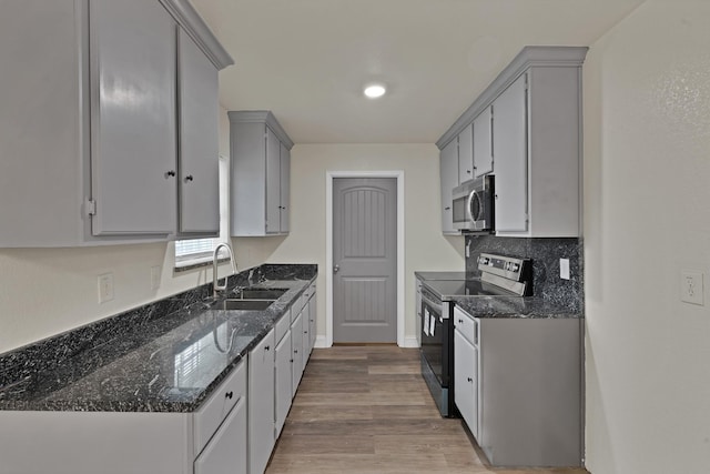 kitchen with tasteful backsplash, dark stone countertops, appliances with stainless steel finishes, wood finished floors, and a sink