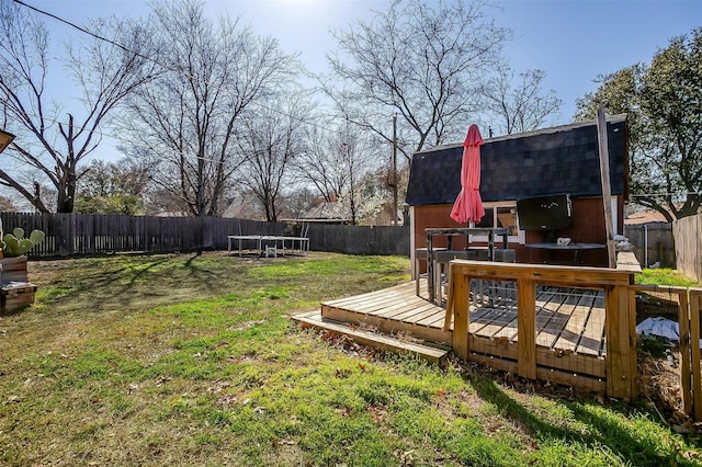 view of yard featuring a deck, a trampoline, and a fenced backyard