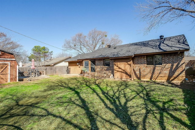 rear view of house featuring fence, a yard, an outdoor structure, a storage unit, and brick siding