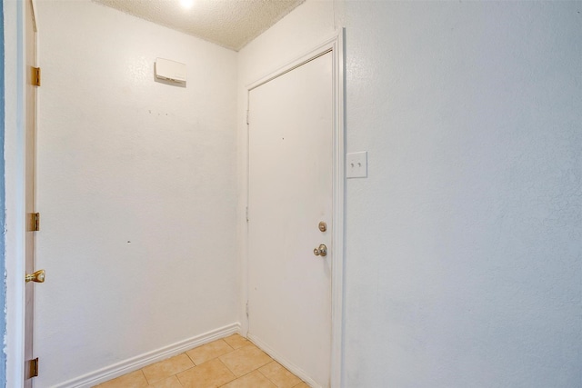 doorway featuring baseboards, a textured ceiling, and light tile patterned flooring