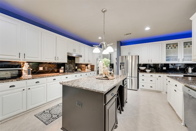 kitchen with under cabinet range hood, a center island, white cabinetry, appliances with stainless steel finishes, and glass insert cabinets