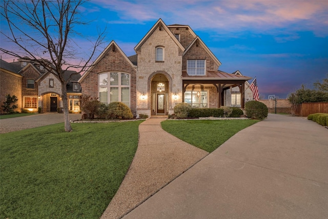 french country style house featuring fence, brick siding, a front lawn, and a standing seam roof