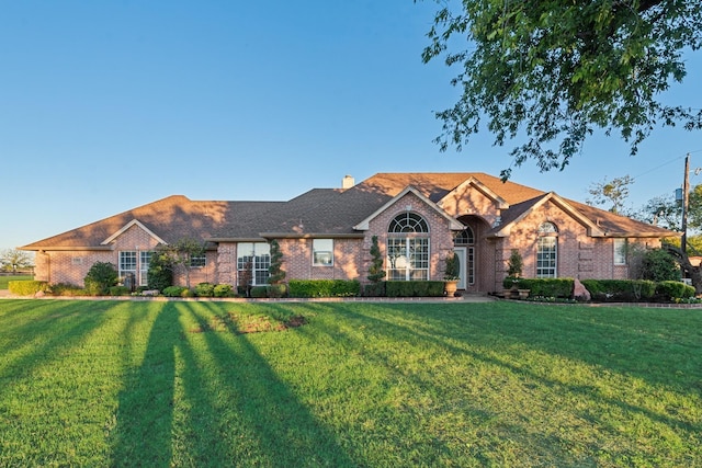 view of front of home with brick siding, a chimney, and a front yard