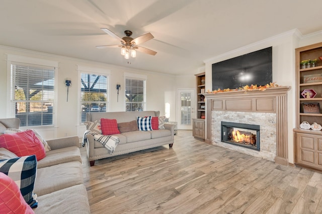 living area featuring light wood-type flooring, a ceiling fan, built in features, crown molding, and a tile fireplace