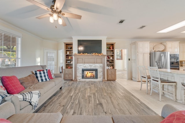 living room with visible vents, light wood finished floors, a glass covered fireplace, and ornamental molding