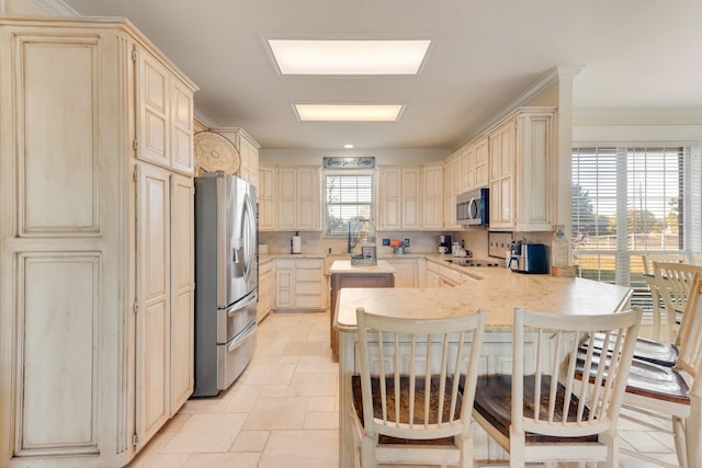 kitchen with light countertops, a kitchen breakfast bar, appliances with stainless steel finishes, a peninsula, and cream cabinetry