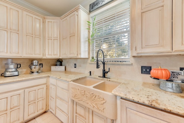 kitchen featuring a sink, light stone counters, backsplash, and cream cabinets