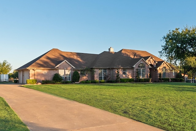 view of front of home with driveway, a front lawn, an attached garage, brick siding, and a chimney