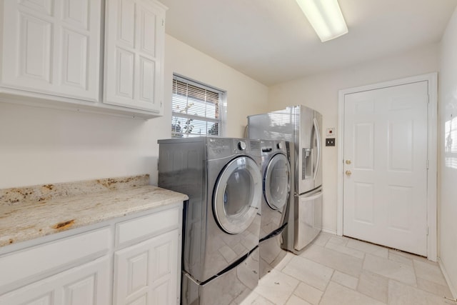 washroom featuring baseboards, cabinet space, stone tile floors, and washer and clothes dryer