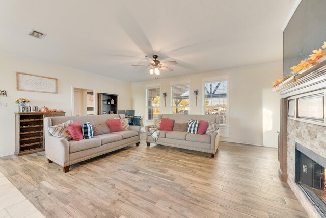 living area featuring visible vents, ornamental molding, a fireplace, light wood-style floors, and a ceiling fan