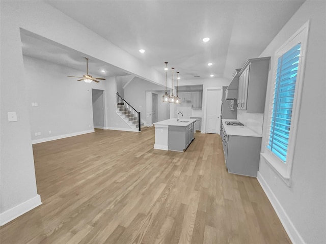 kitchen with gray cabinetry, a center island with sink, a sink, light wood finished floors, and light countertops