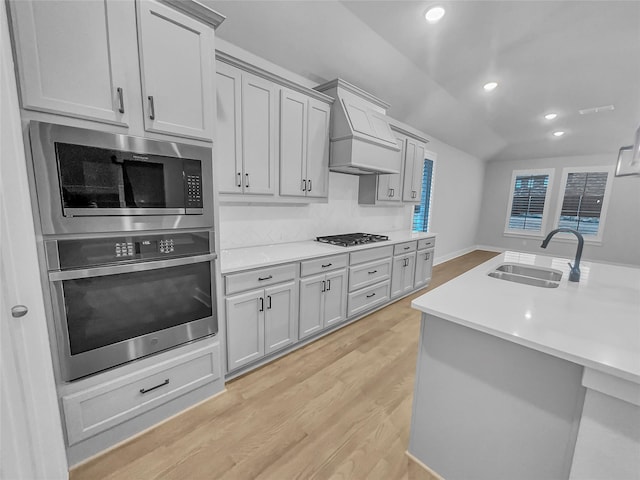 kitchen with premium range hood, a sink, stainless steel appliances, light countertops, and light wood-type flooring